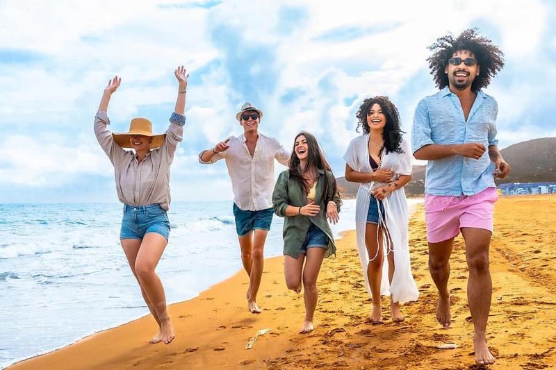 Group of happy multiracial friends enjoying summer vacation, cheerfully running by the ocean shoreline, feeling freedom and happiness together during leisure time