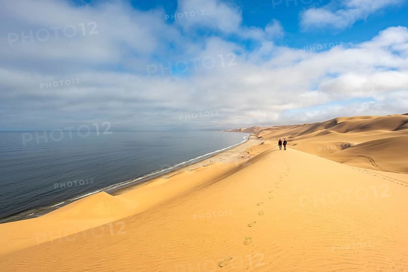 Tourists on a dune, sand dunes and sea in morning light, Atlantic coast and Namib desert, impressive desert landscape, Sandwich Harbour, Namib Naukluft Park, Namibia