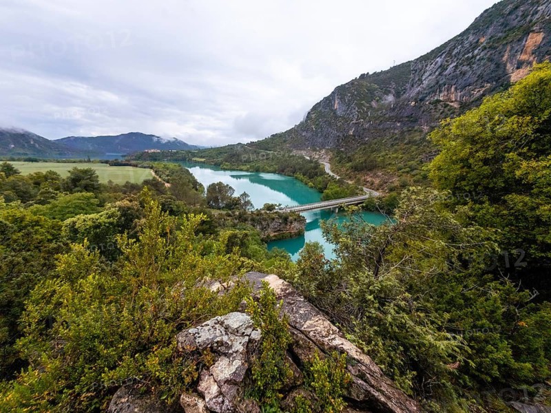 Entremon gorge revealing the cinca river's turquoise water winding through lush green mountains and fields, with a road bridge spanning the river under a cloudy sky in the spanish pyrenees