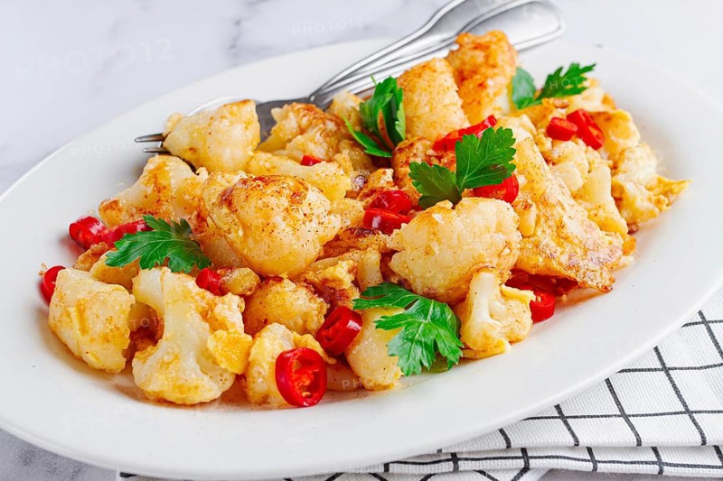 Cauliflower dish, with chili pepper and parsley, on a white plate served on a marble countertop