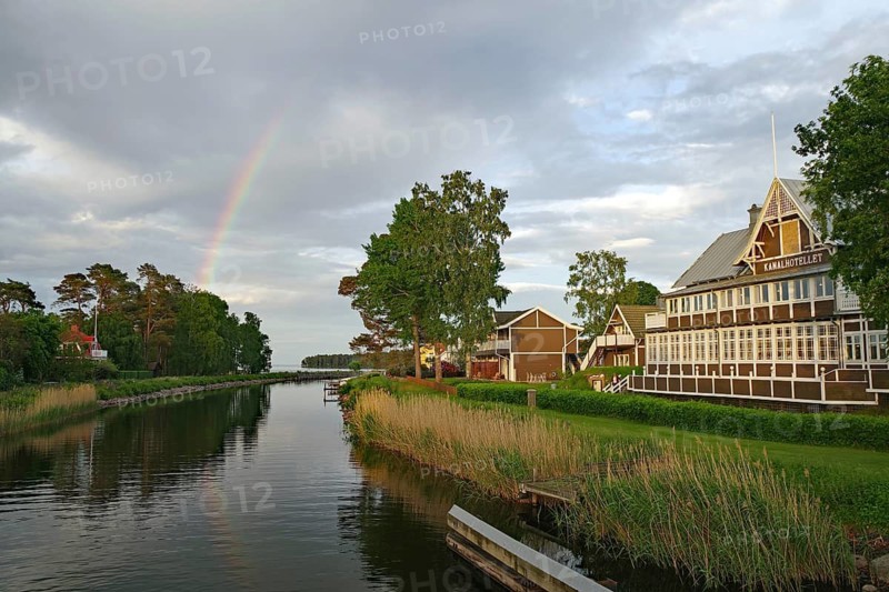 Beautiful rainbow over a quiet river landscape with traditional wooden buildings and green trees, old hotel, Karlsborg, Västra Götalands län, Sweden