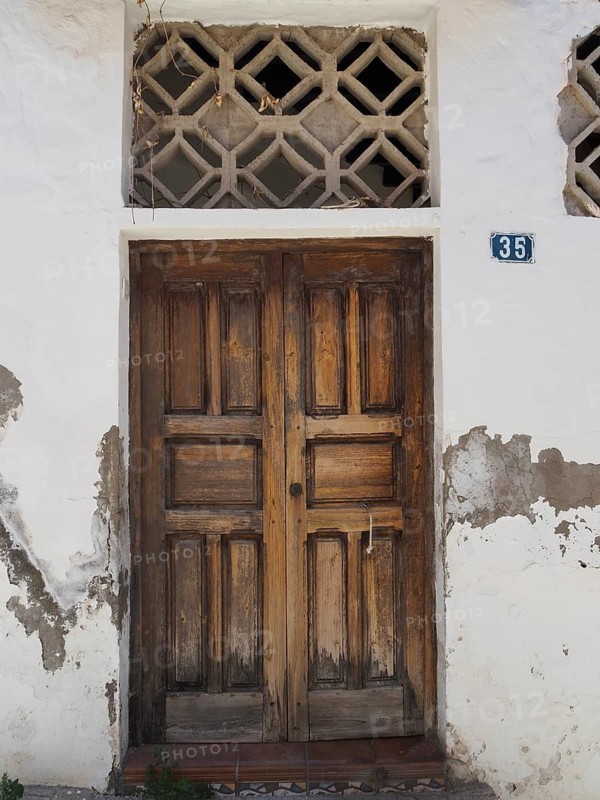 Old wooden door in white wall with peeling paint and house number, Fataga, Barranco de Fataga, Gran Canaria, Spain