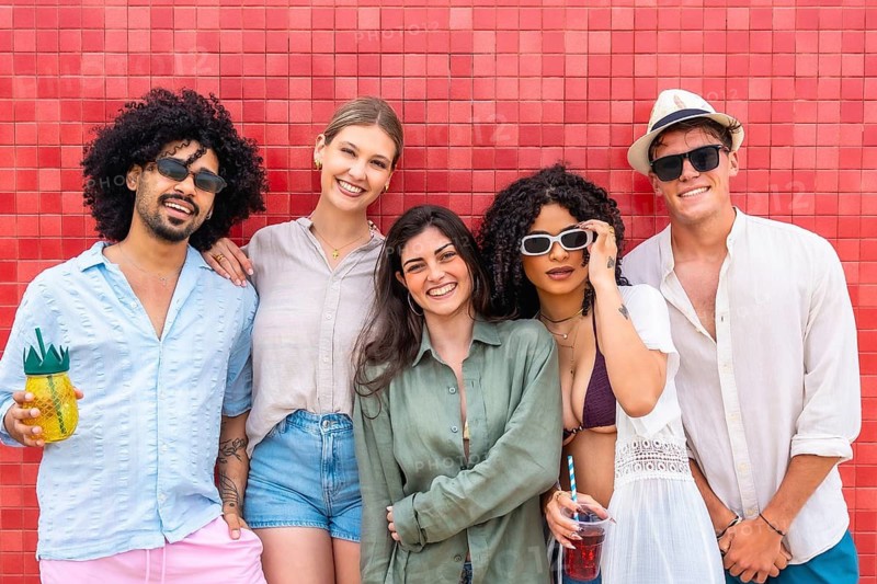 Diverse group of young friends in casual summer clothes laughing and posing against a bright red wall, enjoying inclusive, carefree social time and vibrant urban style