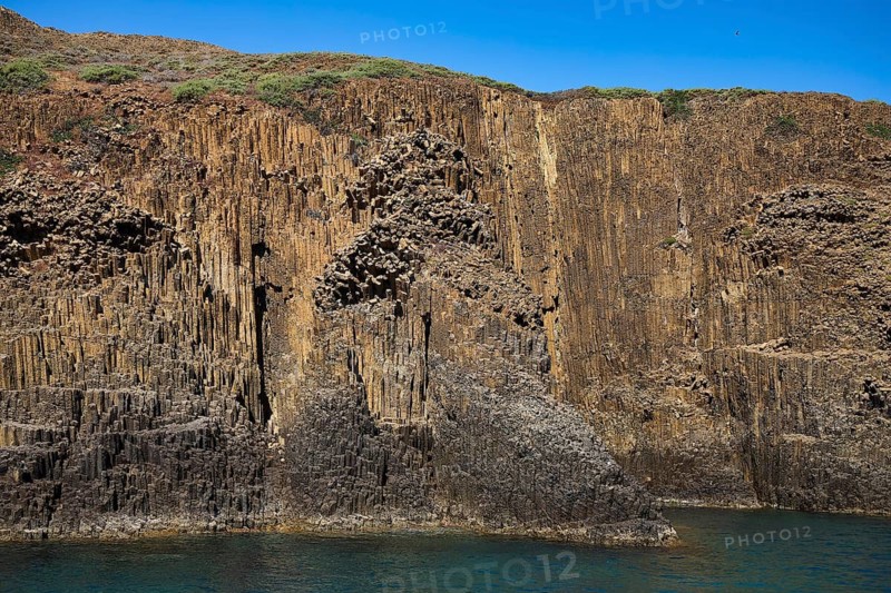 Steep rock wall with basalt columns and sparse vegetation near the sea, Glaronisia, Glaronesia, Milos, islets, hexagonal basalt columns, north of Milos, excursion destination by boat, Cyclades, Greek Islands, Greece