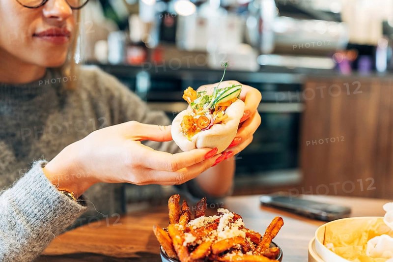 Woman savoring a gourmet bao bun in a modern cafe setting