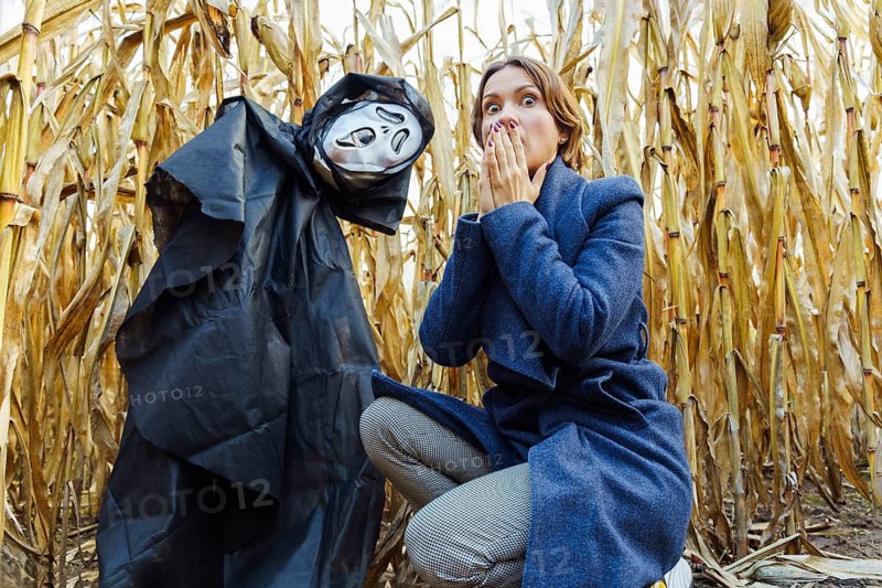 A woman with a frightened face squatted near an effigy with a death mask in a cornfield on Halloween