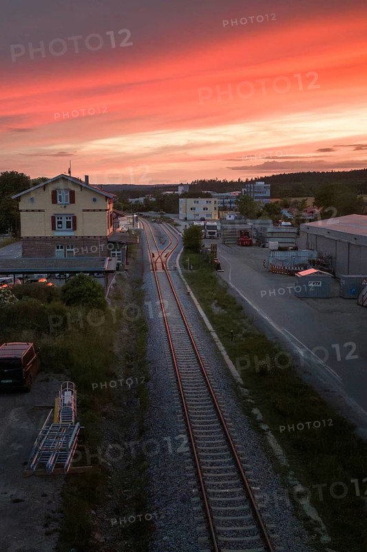 Railway tracks stretch through an industrial park dominated by a colorful sunset, Hermann Hesse Railway, Althengstett, Calw district, Germany