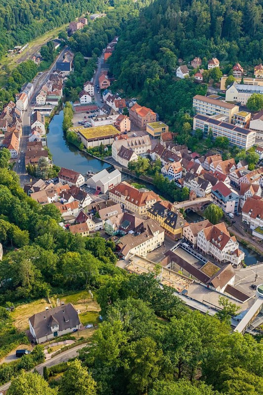 A bird's-eye view of a city with a river, surrounded by green hills and forests, Hermann Hesse Railway, Calw, Germany