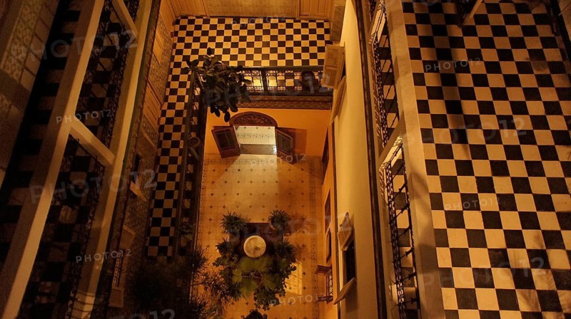 From above, a checkerboard-like Moroccan courtyard of a riad in the old town, Medina, with balcony and plants at night, Marrakech, Morocco
