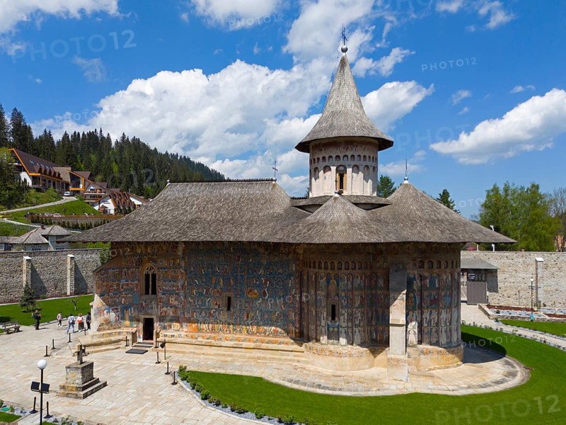 Historic Orthodox church with painted façade, nestled in rural and wooded surroundings under blue sky, aerial view, Saint George Monastery, Voronet Monastery, Voronet Monastery, UNESCO World Heritage Site, Suceava County, Bukovina Region, Romania