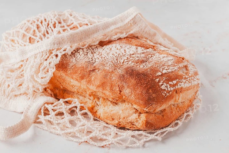Freshly baked rye bread, ciabatta, in a mesh bag, on a marble light table, natural light