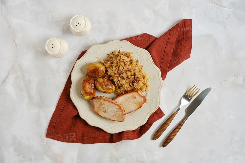 Pork chops with roasted potatoes and sauerkraut on white plate. Meal is placed on red napkin. Salt and pepper shakers are positioned nearby on table