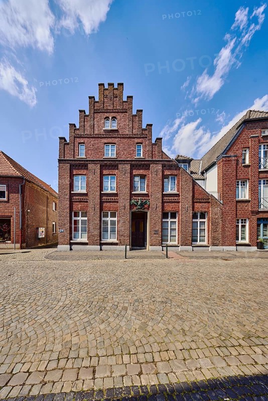 Historic city center, historic brick building Schwarzer Adler, façade with windows, staggered gable, barrier bollard, street, paving stones, blue sky, cumulus clouds, Feldstraße, Wachtendonk, Kleve district, North Rhine-Westphalia, Germany