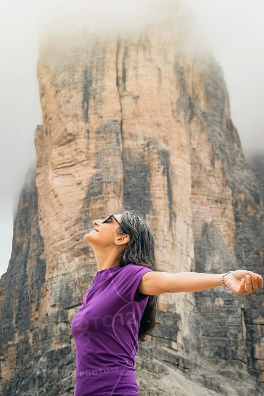 Woman outstretching arms breathing deep misty towering rock wall backdrop Tre Cime di Lavaredo Dolomites Alps Italy summer landscape