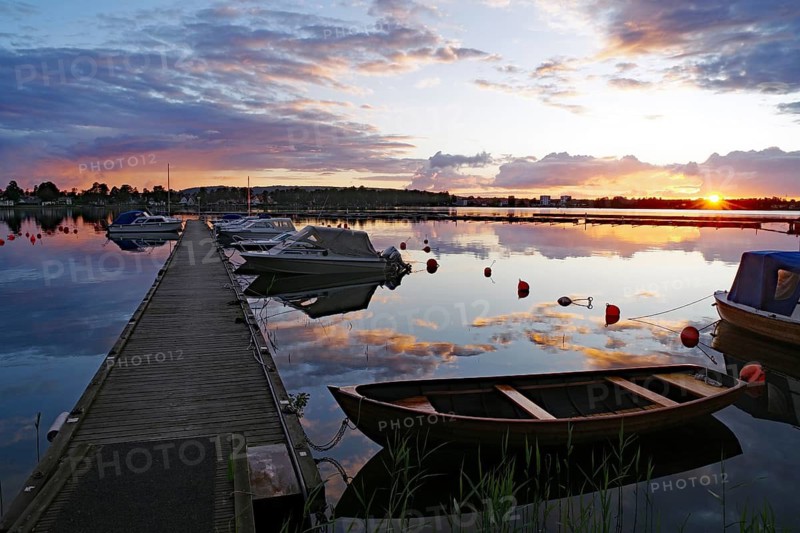 Calm sunset at the harbor with boats and a wooden pier, the water reflecting the colorful sky, Karlsborg, Västra Götalands län, Sweden