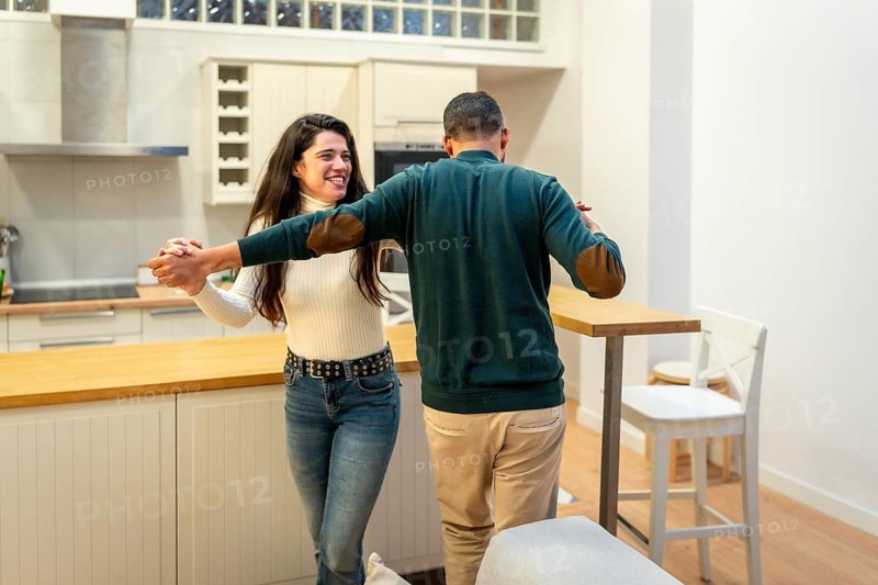 Happy couple swaying with joy and holding hands, enjoying a romantic moment while dancing playfully in their modern kitchen, symbolizing togetherness, connection, and domestic fun