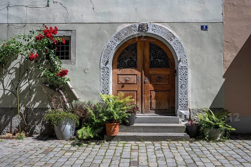 Historic wooden portal with stone round arch and stone steps. Entrance of an old house with blooming red roses and potted plants on the façade in the old town of Lindau am Lake Constance, Swabia, Bavaria, Germany