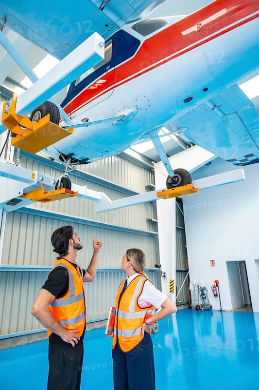 Aviation technician and pilot collaborate, performing a thorough pre flight inspection and maintenance check on a small aircraft suspended on a specialized lift inside an industrial hangar