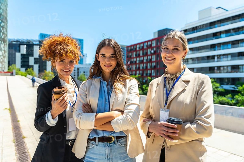 Three confident businesswomen standing together and smiling in a modern city setting, representing diverse professional collaboration, teamwork, and female empowerment in the corporate world
