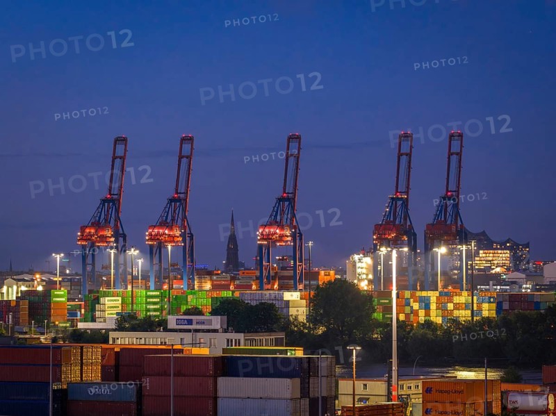 View over the Container Terminal Burchardkai (CTB) in Hamburg-Waltershof with container gantry cranes and stacked freight containers as well as the Elbe Philharmonic Hall concert hall and the tower of St. Nikolai Church in the background at blue hour, Hamburg, Germany