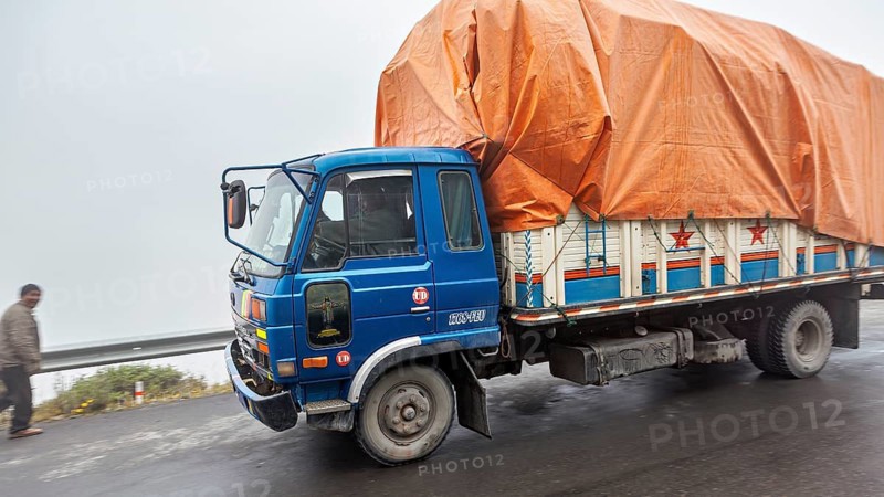 Blue truck with orange tarpaulin drives on a foggy road, isolated people visible, truck and road traffic towards Rurrenabaque through the Andes on the Road of Death in Bolivia
