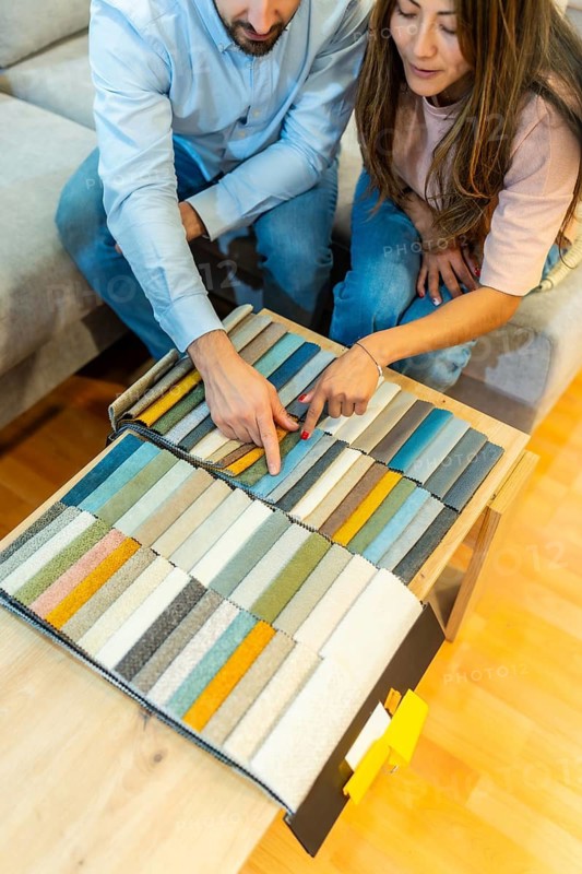 Young couple selecting fabric swatches for sofa upholstery. Sitting together and pointing at different color and texture options from a detailed display. Planning their home decor and interior design