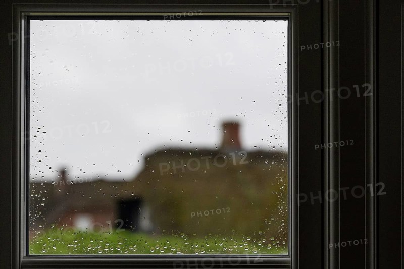 View through a window pane with raindrops beading, blurred traditional thatched Danish houses in the background, Houvig, North Sea, Denmark