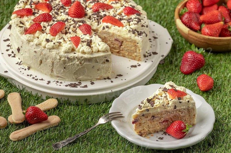 Sliced cake with strawberries, cream and chocolate on a plate on grass