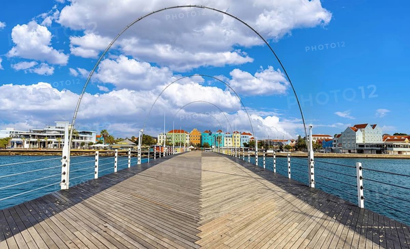 View from the wooden deck of the Queen Emma Bridge towards the iconic colorful colonial architecture of the Punda district in Willemstad, Curacao under a blue sky with clouds in Caribbean