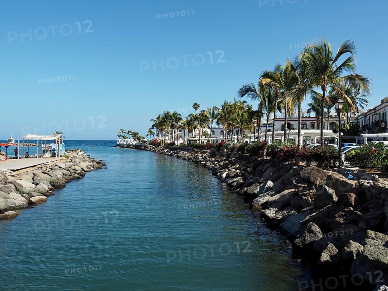 A quiet water channel lined with palm trees and rocks overlooking the sea, Puerto de Mogan, Gran Canaria, Spain