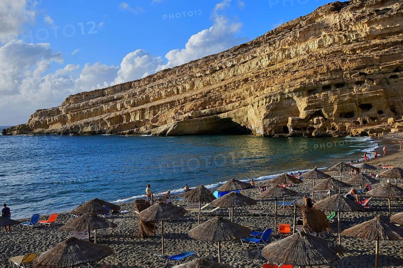 Neolithic caves, former hippie paradise, visited beach with colorful umbrellas against huge cliffs and sandy shore, Matala, south coast, Crete, Greek Islands, Greece