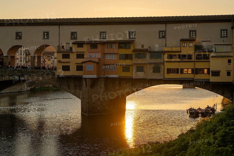 Sun rays reflect on the Arno River, crowd on the historic Ponte Vecchio, evening mood, old town, Florence, Tuscany, Italy