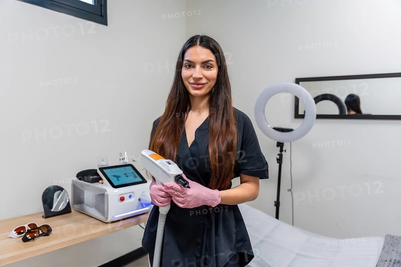 Female professional in a clinic holding a modern laser device, ready for aesthetic treatments like tattoo removal and hair removal, creating a sense of expertise and modern care