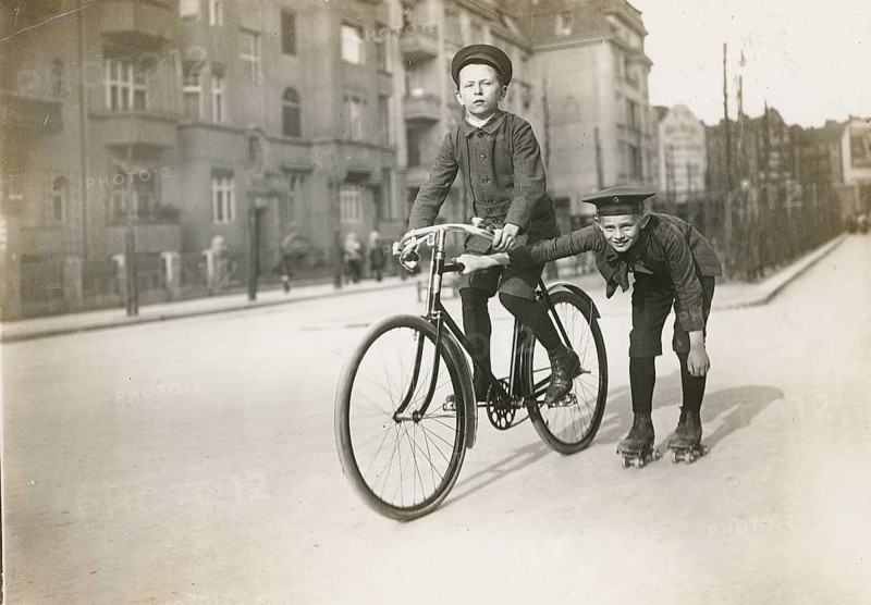 Berlin, roller skating, children, girls, boys, leisure, fun, middle class, A boy rides a bicycle on the street, another sticks to a bicycle on roller skates, Philipp Kester, around 1906