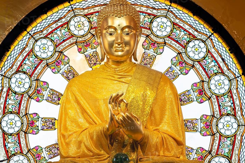In the main chedi of Wat Phra That Sorn Kaew, the gilded Buddha statue shines out against a luminous glass mandala that fills the space with light and colour. The delicate patterns of the window and the gentle radiance of the robe combine to create an atmosphere of quiet contemplation. This photograph captures the unique harmony of spiritual symbolism, exquisite craftsmanship and meditative tranquillity: the main chedi (Phra That), Wat Phra That Sorn Kaew, Khao Kho Mountains, Phetchabun Province, Isan, Thailand