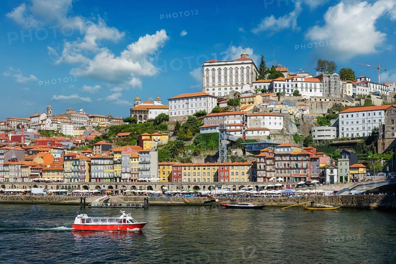Red tourist boat on the Douro River in Porto, Portugal, passes Ribeira old town and its sunny riverfront houses
