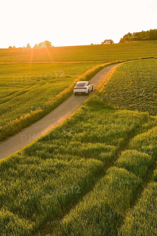 A white car drives on a rural road through green fields at sunset, Tesla Model Y, Gechingen, Calw district, Germany