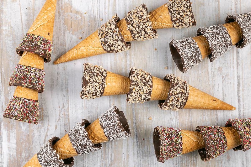 Ice cream cones decorated with nuts and sprinkles on rustic wood