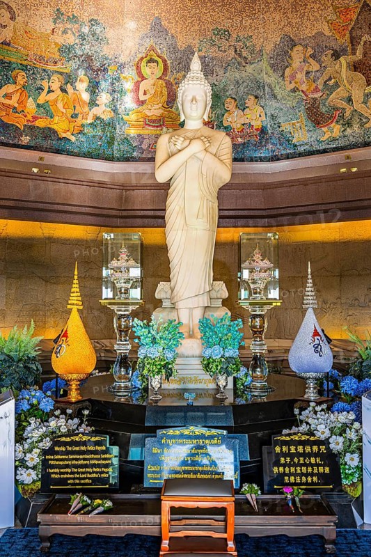 White Buddha statue in meditative posture in front of colorful wall mosaic and artfully designed altar, King Pagoda, Doi Inthanon National Park, Chiang Mai Province, Thailand
