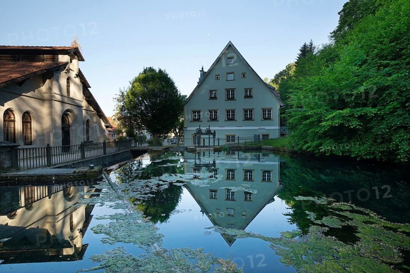 Historic pump station and town house reflected in the clear water of the Brenzursprung karst spring. Koenigsbronn, Baden-Wuerttemberg, Germany