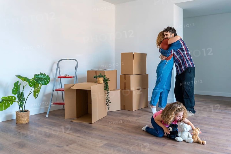 Happy family celebrating moving into a new home, parents embracing with love and joy surrounded by moving boxes, while their daughter plays with stuffed animals