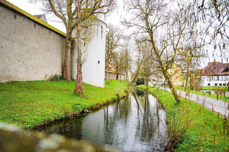 Small river along an old castle wall, surrounded by trees and green grass, Isny, Allgäu, Bavaria, Germany