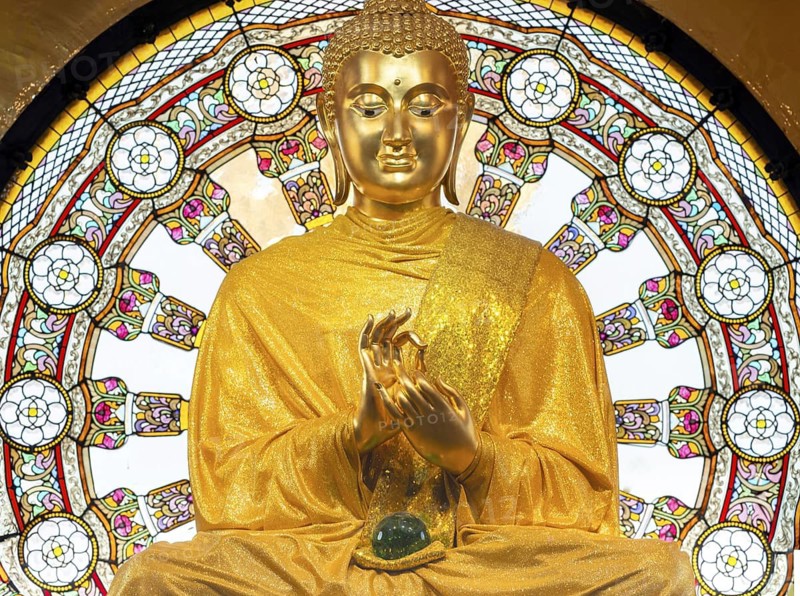 In the main chedi of Wat Phra That Sorn Kaew, the gilded Buddha statue shines out against a luminous glass mandala that fills the space with light and colour. The delicate patterns of the window and the gentle radiance of the robe combine to create an atmosphere of quiet contemplation. This photograph captures the unique harmony of spiritual symbolism, exquisite craftsmanship and meditative tranquillity: the main chedi (Phra That), Wat Phra That Sorn Kaew, Khao Kho Mountains, Phetchabun Province, Isan, Thailand