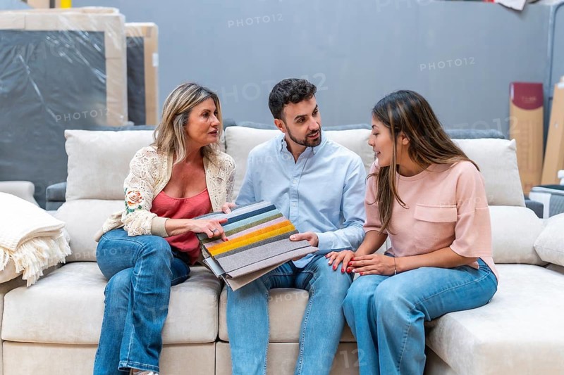 Three customers sitting on a sofa, discussing and choosing textile color and material swatches from a stack, making interior design decisions for their new home