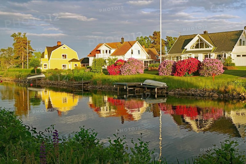 Colourful houses are reflected in calm waters surrounded by blooming gardens in spring, Göta Canal, Karlsborg, Västra Götalands län, Sweden