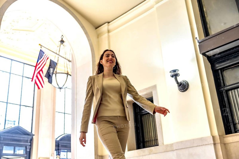 Confident businesswoman with a warm smile walking through a grand building interior in manhattan, representing success, career advancement, and a powerful professional presence
