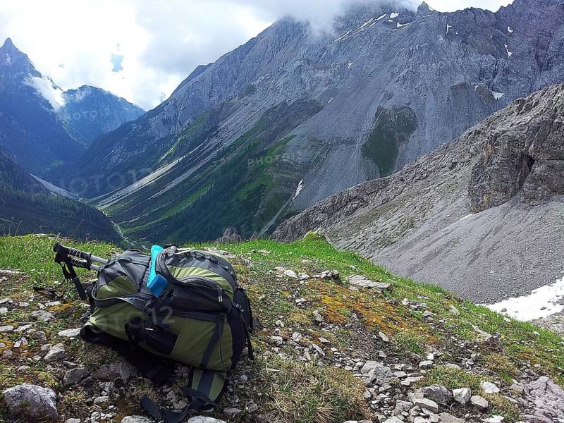 Backpack on mountain meadow with a view of steep, rocky mountain landscape, E5, hiking in the Alps, crossing the Alps, Austria