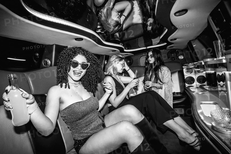 Group of diverse friends celebrating and enjoying drinks inside a luxurious limousine interior during a party, reflecting excitement and a lavish nightlife experience