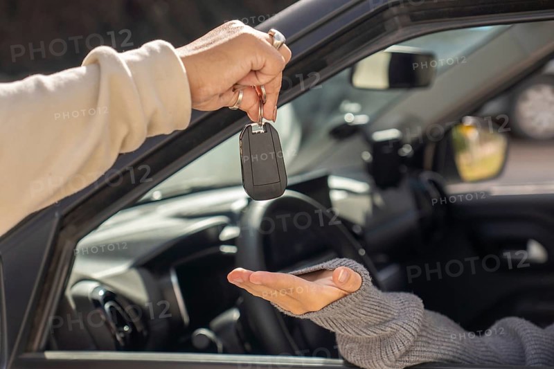Close-up of hand giving car key to student driver seated behind the wheel, key exchange, car interior, driving lesson concept