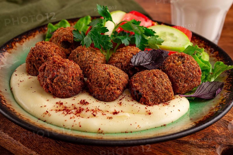 A plate holds falafel balls, tahini, salad with tomatoes and cucumbers, and a drink. The setting is warm and inviting, perfect for a midday meal with fresh ingredients
